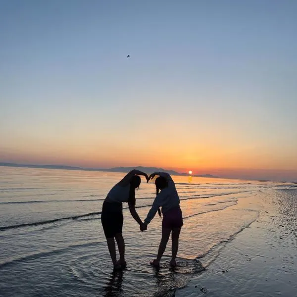 Two girls forming a heart shape on a beach at sunset